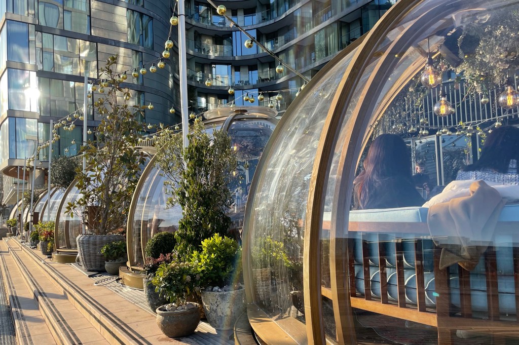 3 glass and metal-framed igloos in a row under a canopy of hanging lights.
