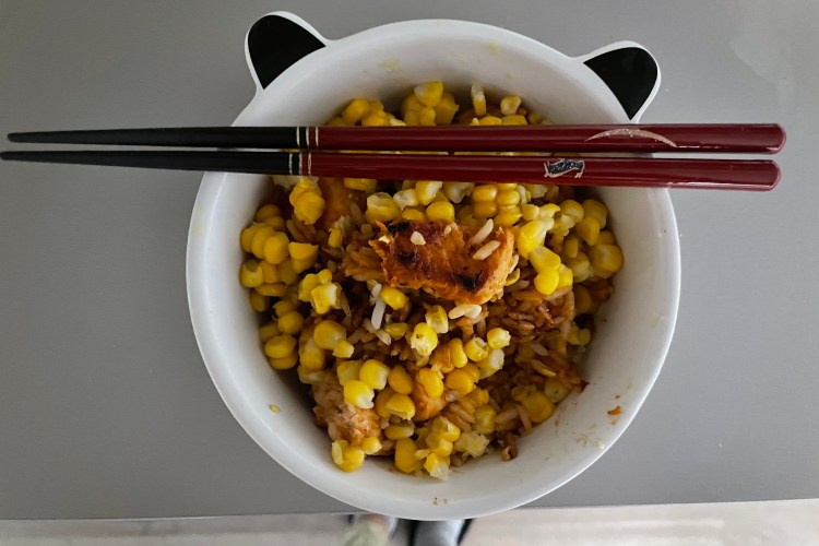 Gochujang chicken in a bowl with egg-fried rice and corn. A pair of chopsticks is balanced on top of the bowl.