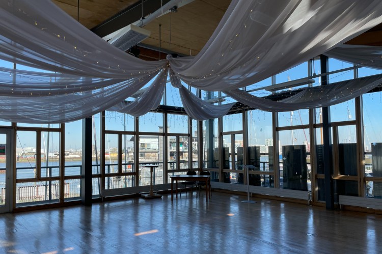 The main event space has a table with two chairs at the far back for marriage certificate signing. Fabric banners with fairy lights are draped from the ceiling to the walls.