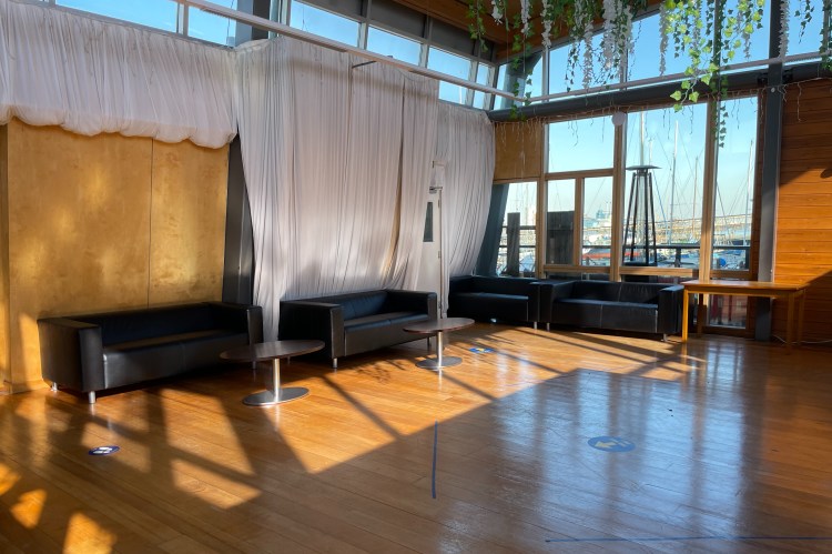 The entrance area has four black couches, a regular table and two coffee tables, as well as fabric draped on inner walls. You can see some of the plants hanging from the ceiling as well.